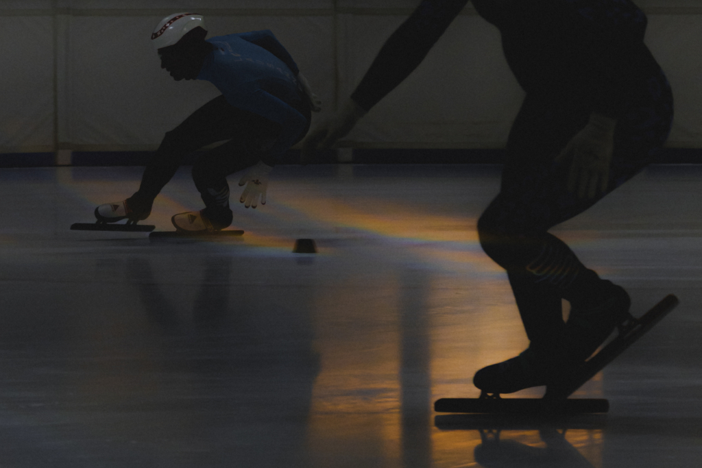 Patineurs de short track dans un virage, avec des reflets lumineux sur la glace à la Vaudoise Arena de Lausanne.